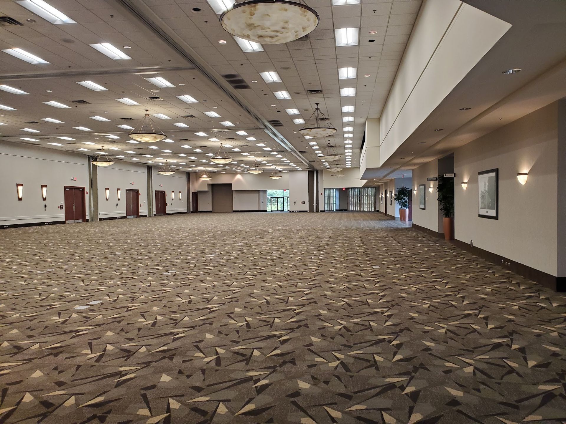 Empty office space with large windows overlooking a city, carpeted floor, and a grid ceiling.