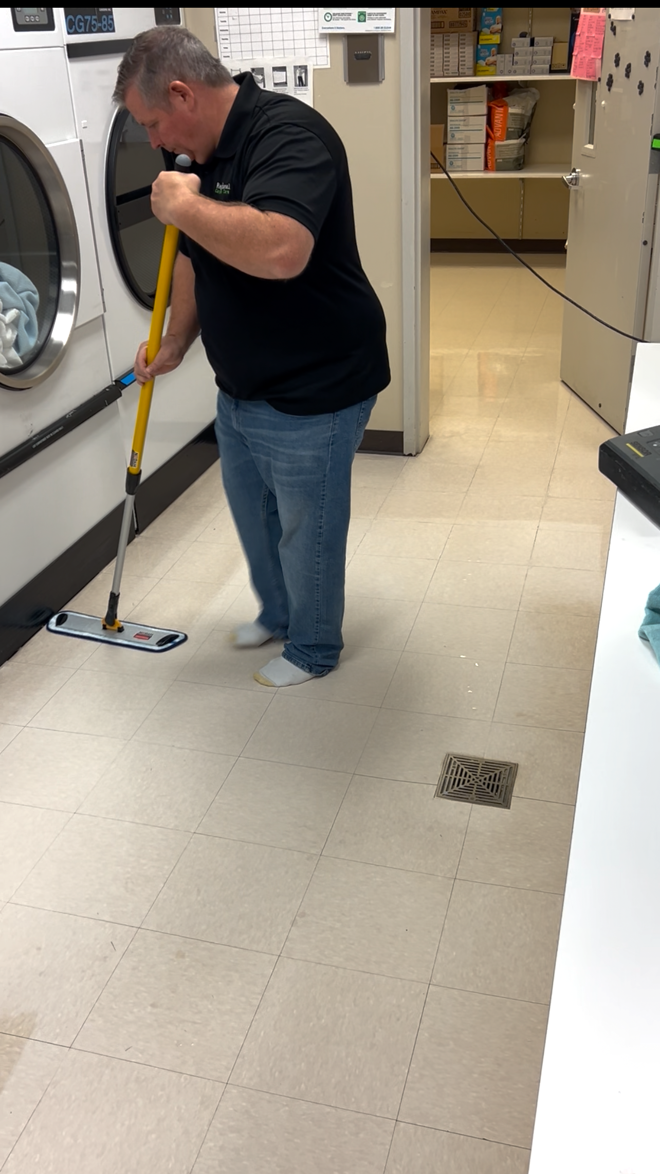 Person operating an orange floor buffer, polishing a shiny floor in a building lobby.