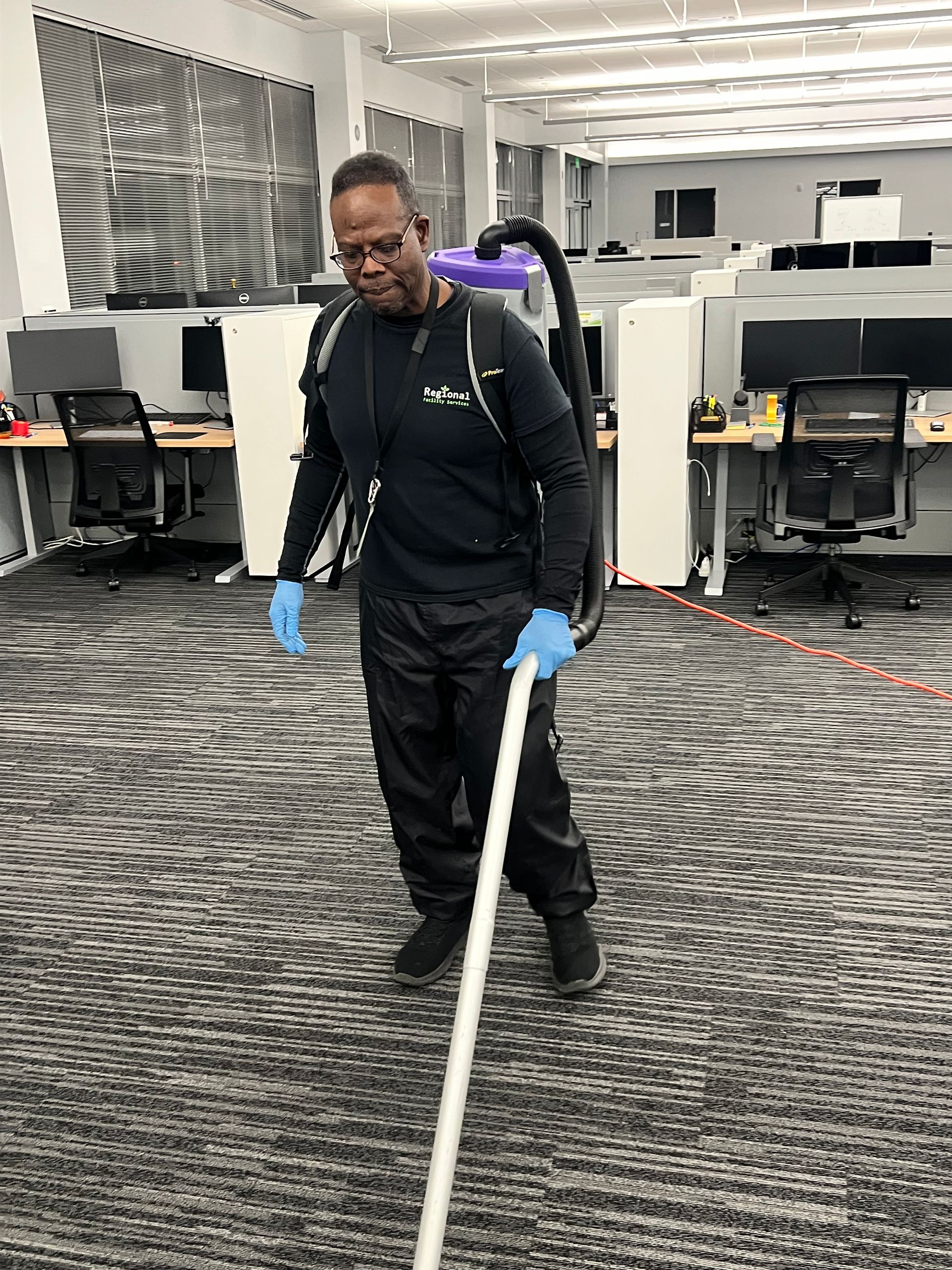 Person in blue scrubs mops a hospital room floor, yellow caution sign nearby.