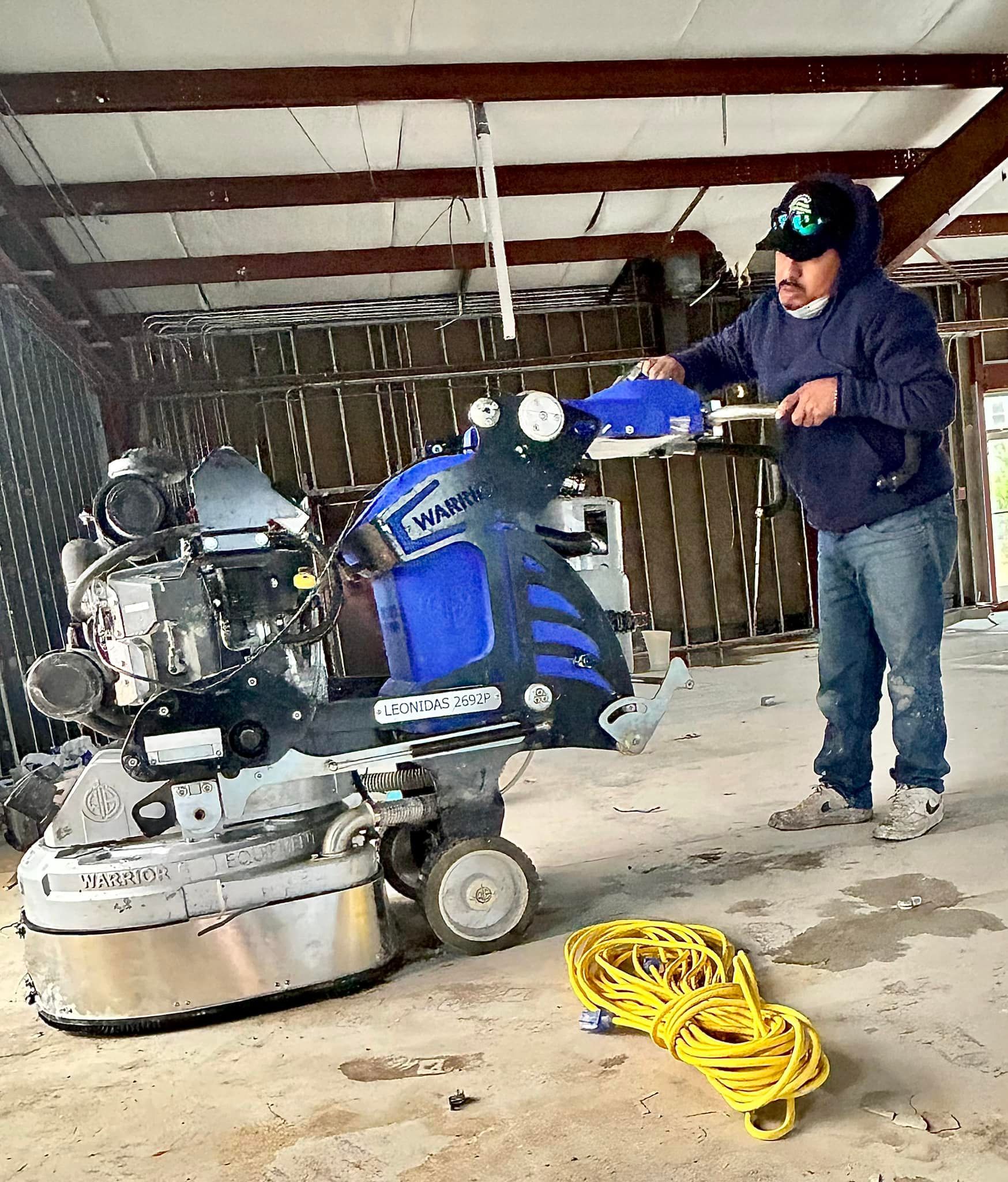Person using a trowel to apply gray coating to a concrete floor indoors.