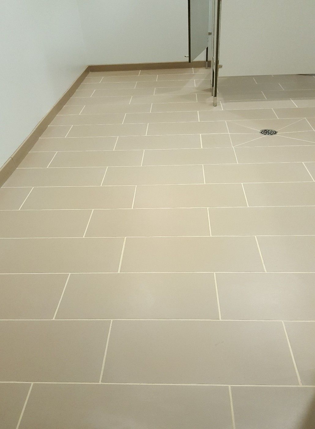 Gloved hand using a trowel to apply grout between white marble tiles.