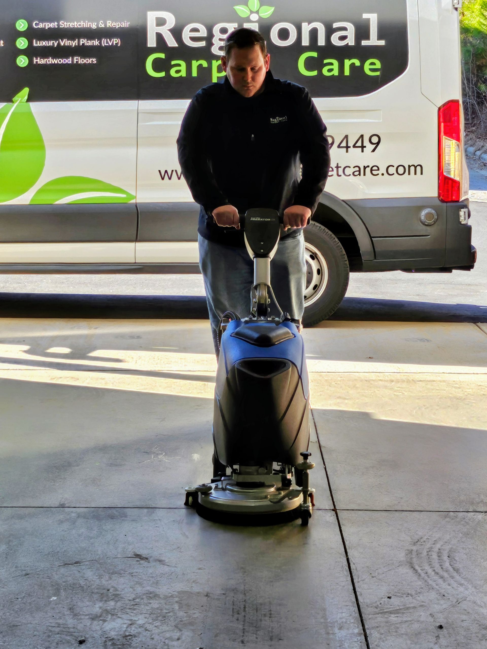 A person cleaning a polished floor with an orange industrial cleaning machine in a room.