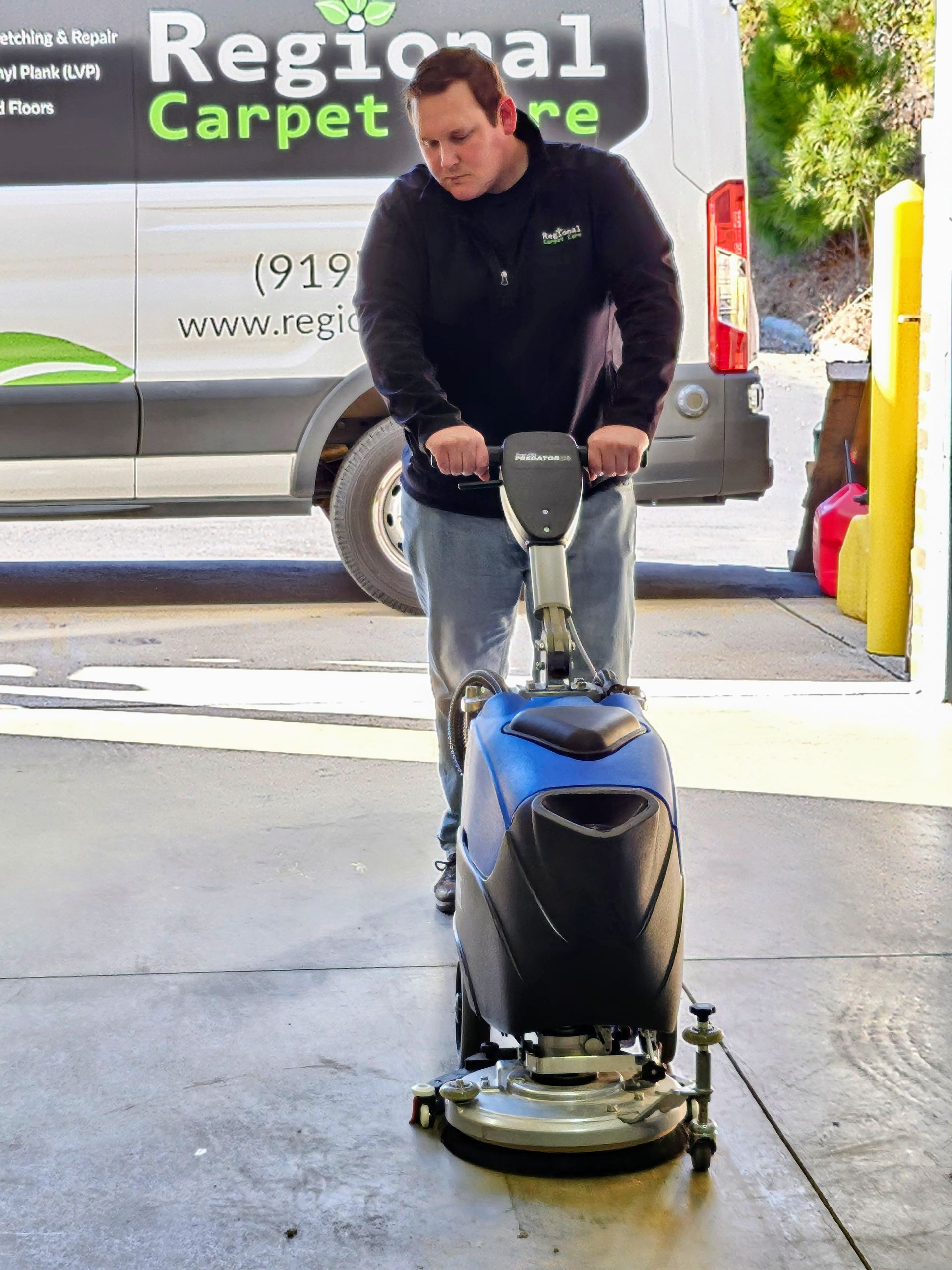 Man operating a floor cleaning machine outside a vehicle with 