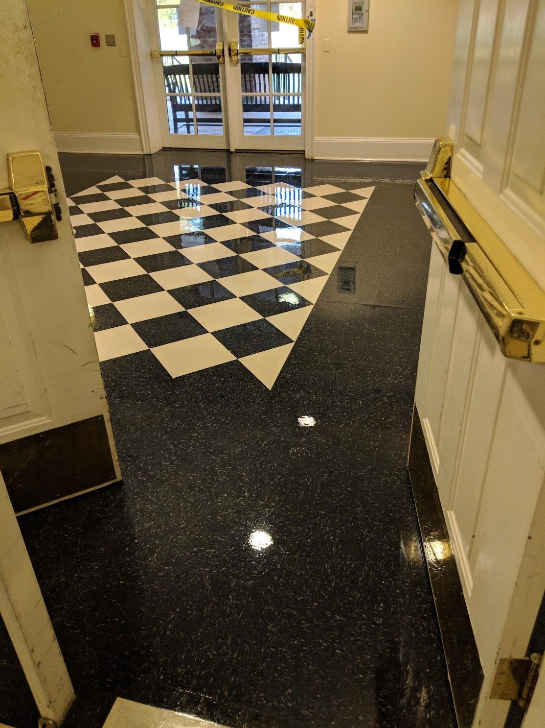 Modern glass building entrance with a concrete patio reflecting the sky.