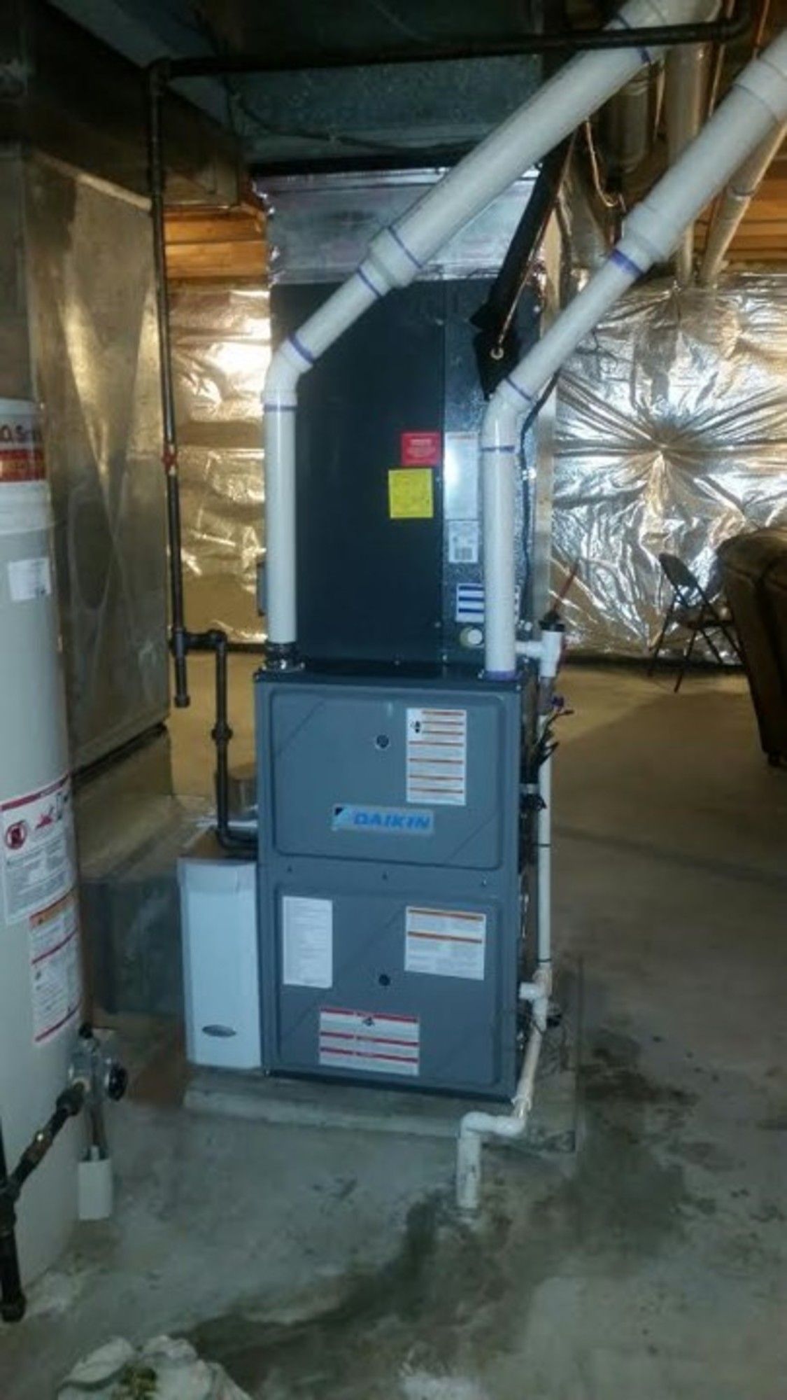 A furnace is sitting in a basement next to a water heater.