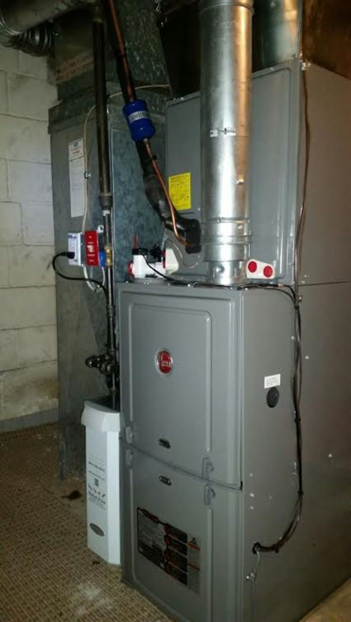 A gray furnace is sitting in a basement next to a white wall.