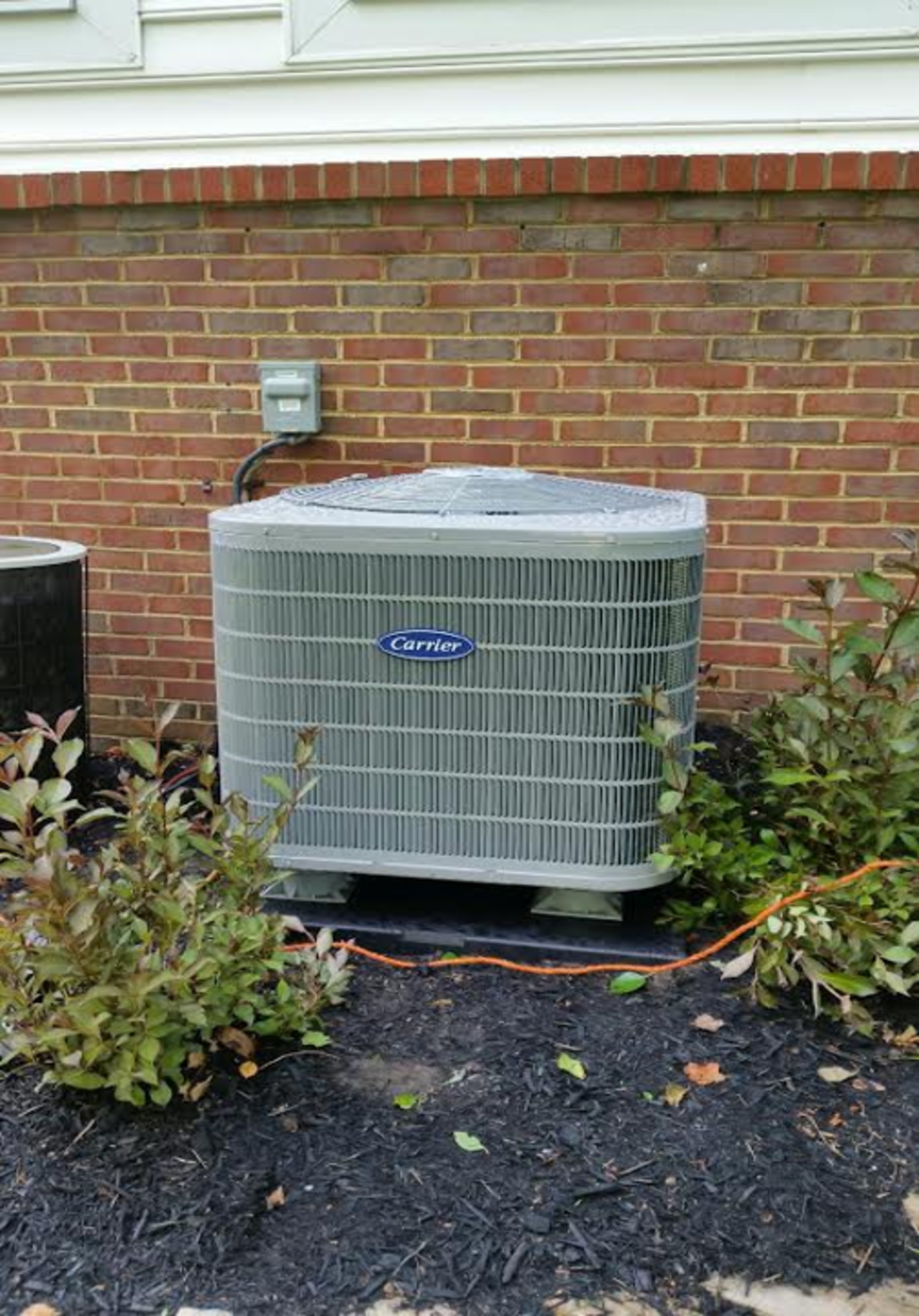 A large air conditioner is sitting on the side of a brick building.