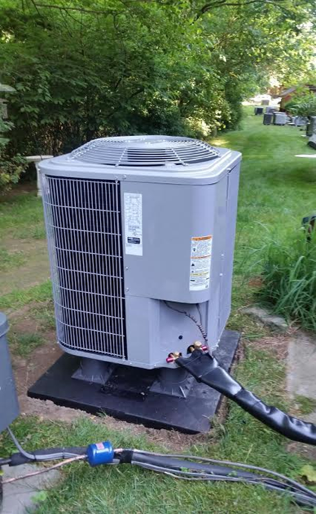 A large air conditioner is sitting on top of a concrete platform in a yard.