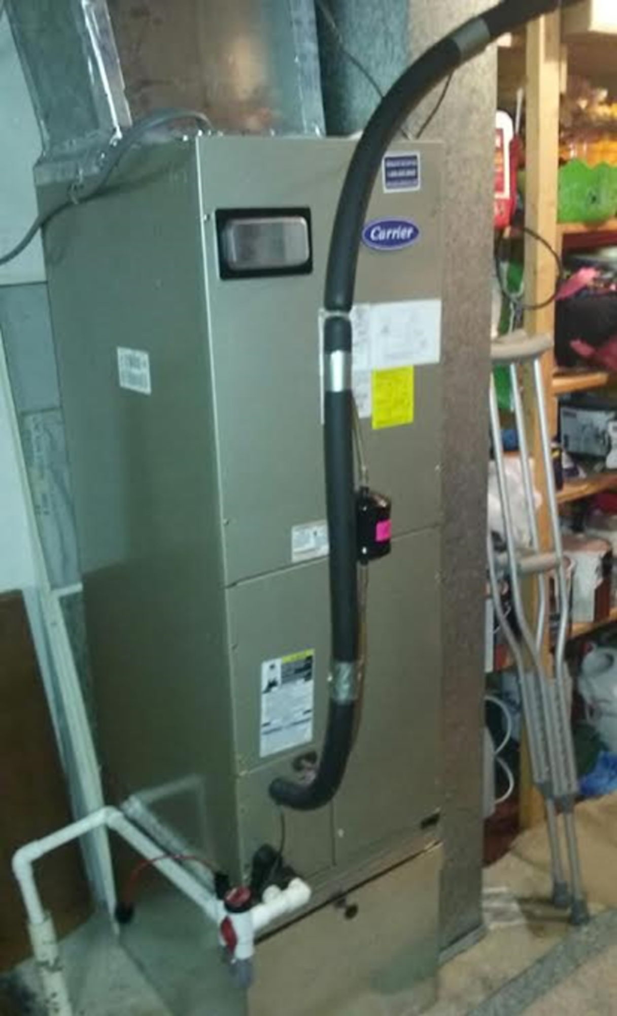 A carrier air conditioner is sitting in a basement next to a ladder.