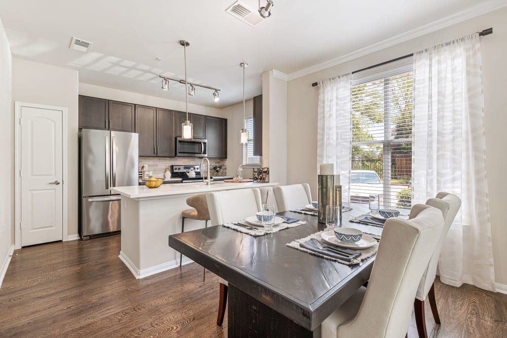 A dining room with a table and chairs and a kitchen in the background at Marquis at The Woodlands in Spring, TX.