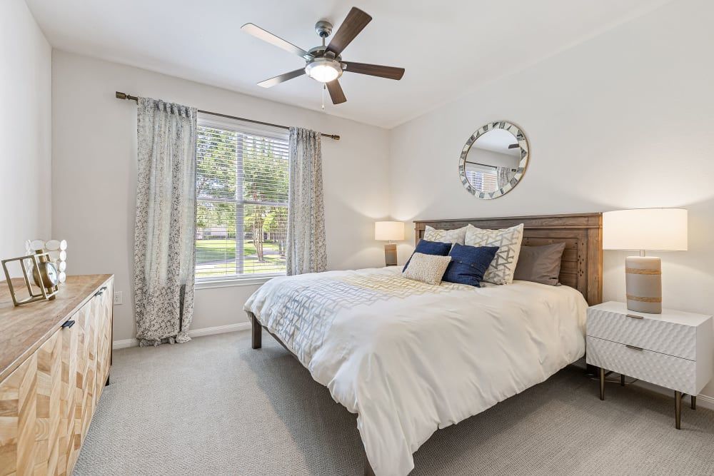 Spacious apartment bedroom with a large bed and a ceiling fan at Marquis at The Woodlands in Spring, TX.