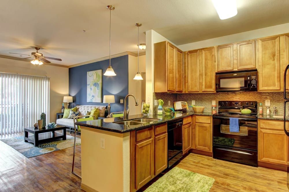 Apartment kitchen with wooden cabinets, a stove, a refrigerator, and a microwave at Marquis at The Woodlands in Spring, TX.