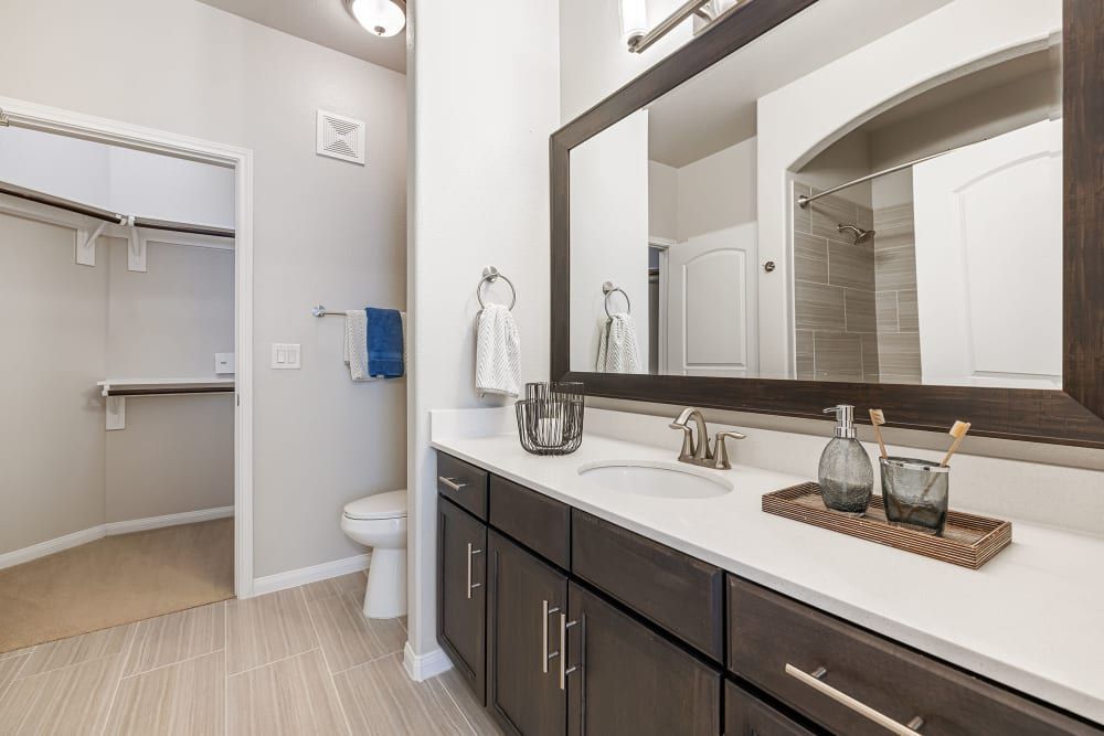 Resort-style bathroom with a sink, toilet, mirror, and walk-in closet at Marquis at The Woodlands in Spring, TX.
