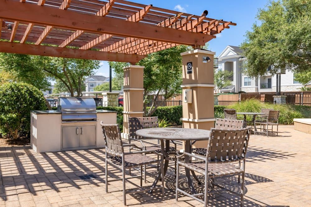 A patio with a table and chairs and a grill under a pergola at Marquis at The Woodlands in Spring, TX.