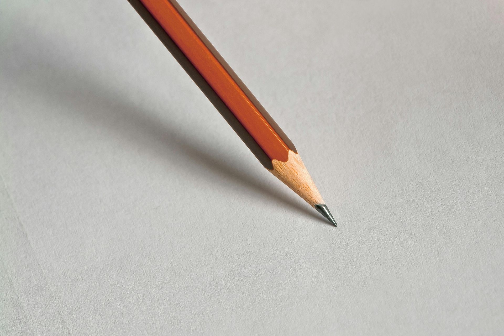 Pencil with a sharpened graphite tip resting on blank, textured white paper.