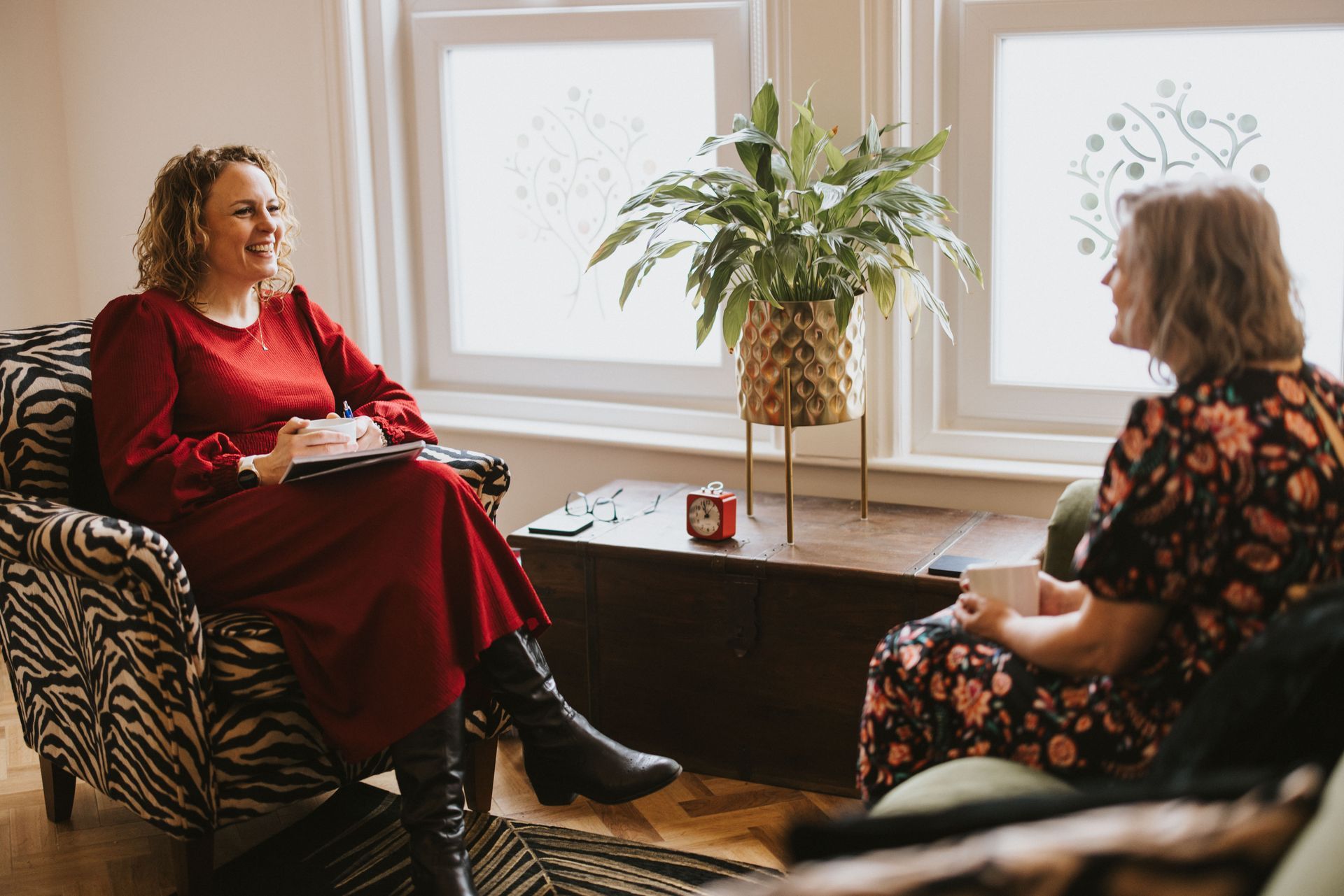 Two women are sitting in chairs talking to each other in a living room.