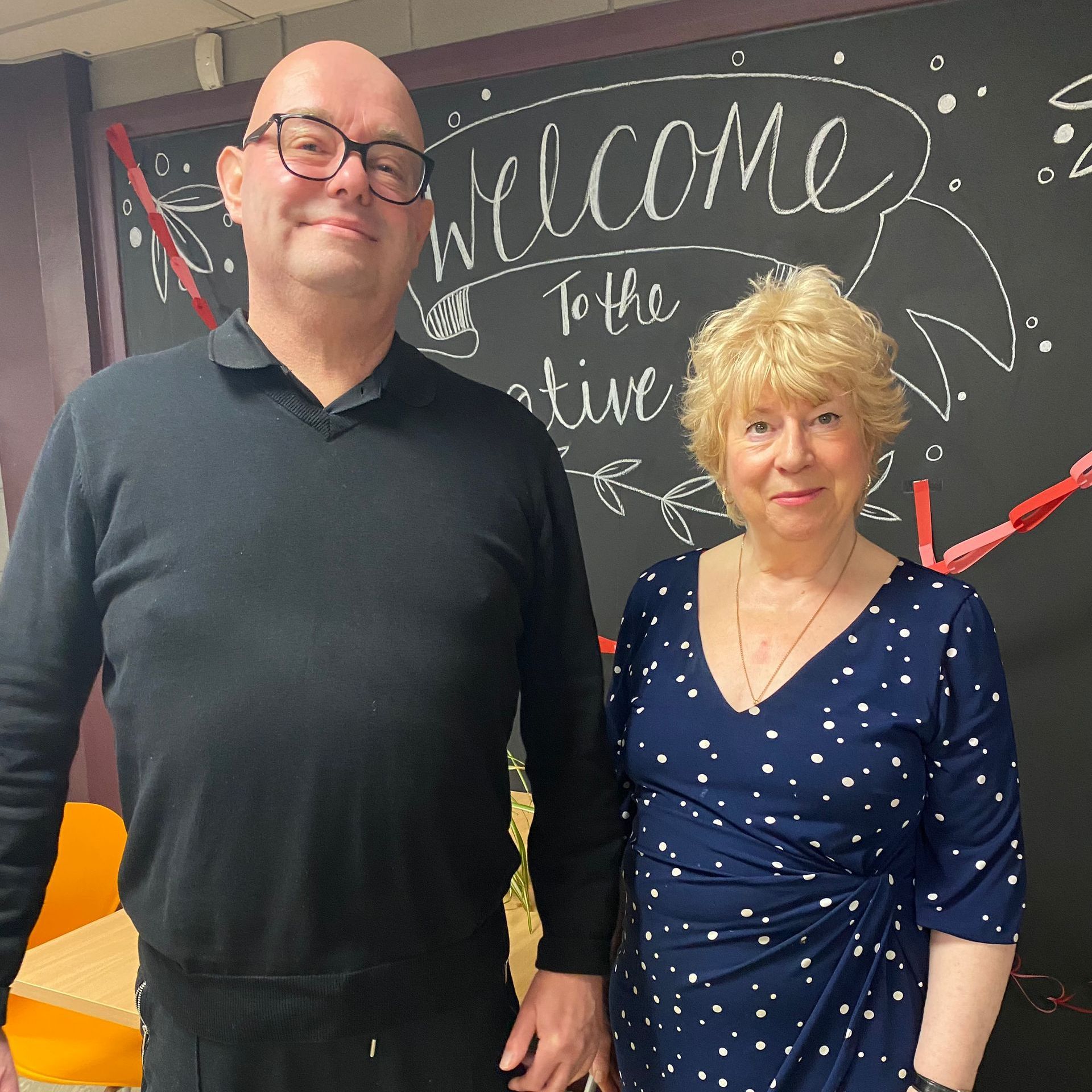 A man and a woman are standing in front of a blackboard that says welcome to the creative