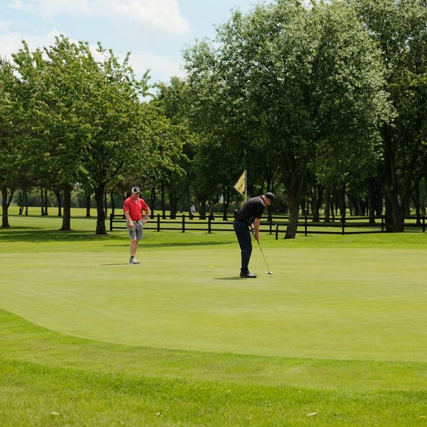 A man in a red shirt is putting on a golf course