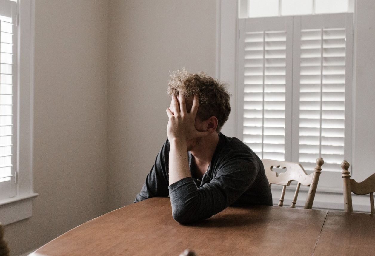 A man is sitting at a table with his hand on his head.