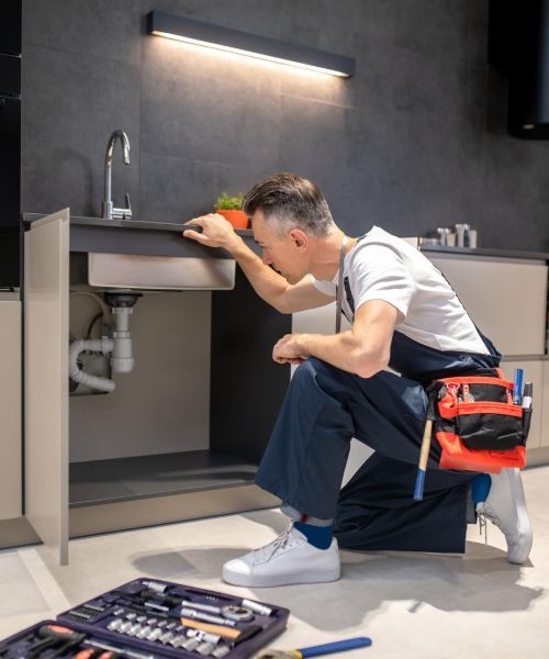 A man is kneeling down under a sink in a kitchen