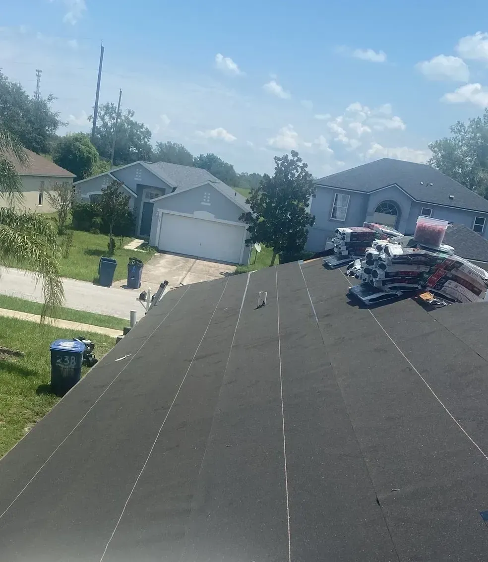 A roof with a lot of roofing materials on it and a house in the background.