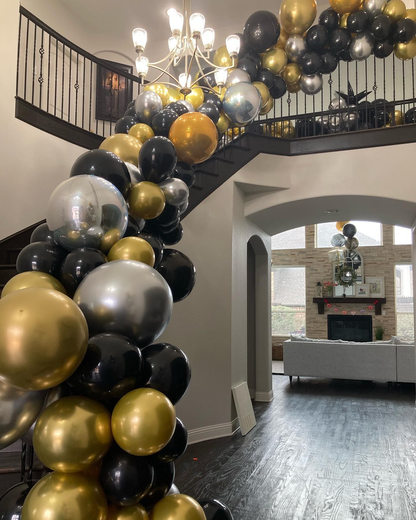 Balloon arch in gold, black, and silver decorates a staircase.