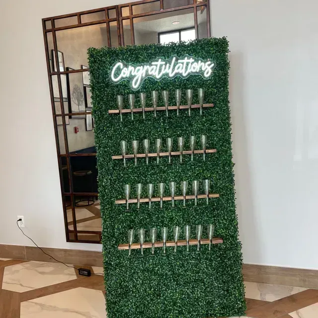 A sign that says `` congratulations '' is surrounded by greenery and wine glasses.