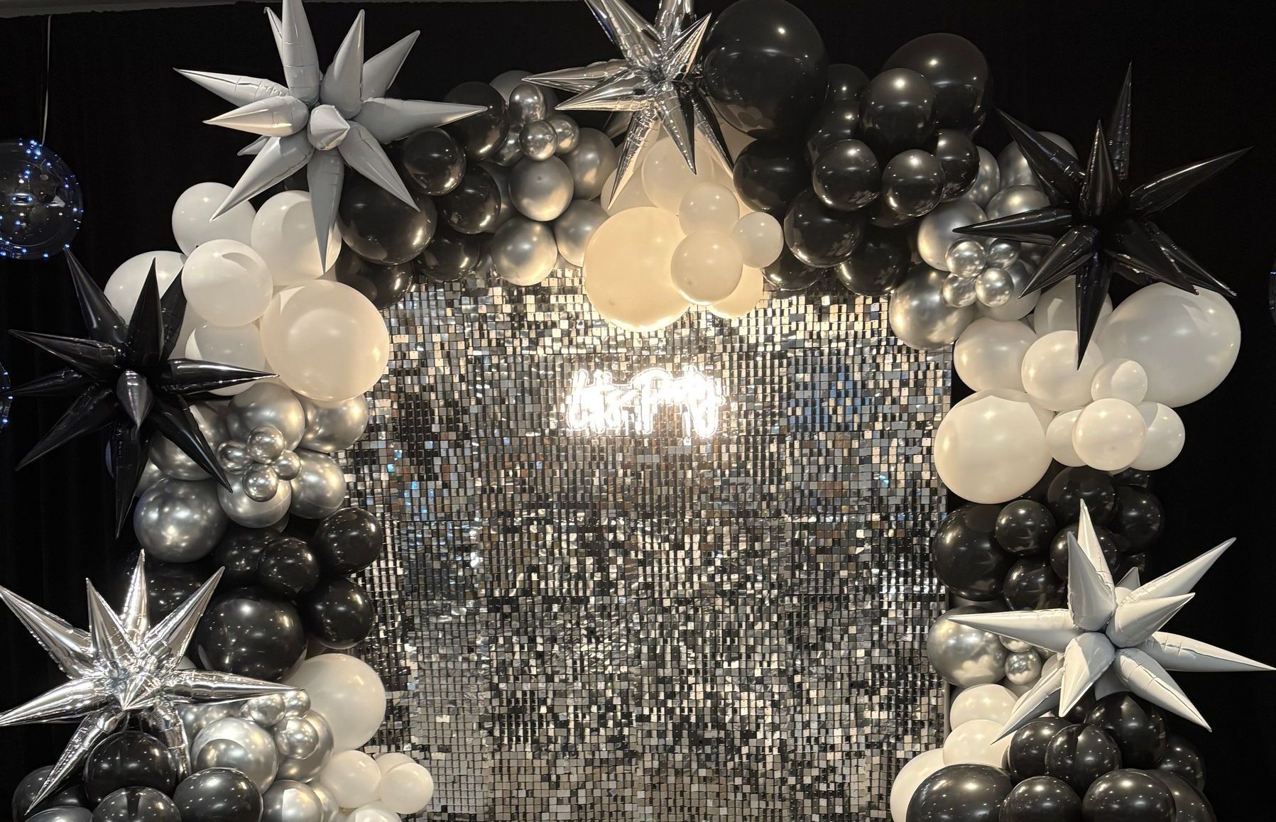A wall filled with black , white and silver balloons and stars.