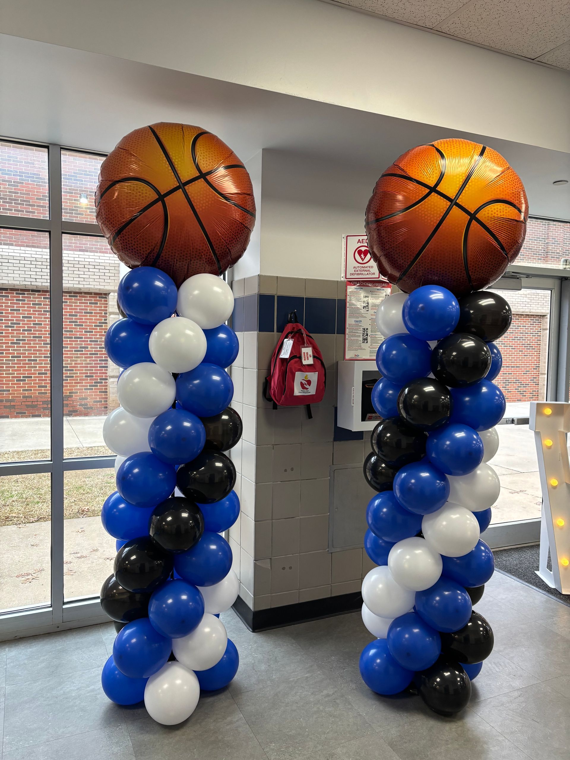 Two basketball-themed balloon columns: orange basketball tops, blue/white/black balloons, in a hallway.