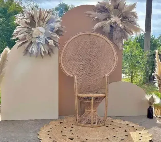 A wicker chair is sitting in front of a wall with flowers on it.