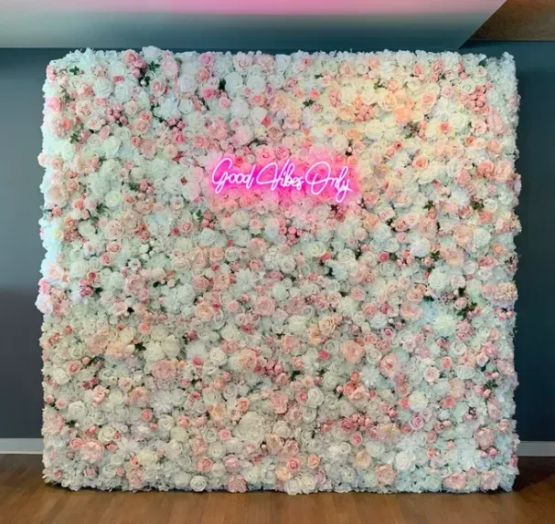 A pink and white flower wall with a neon sign above it.