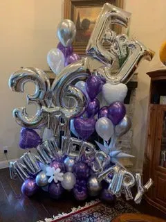 A bunch of purple and silver balloons in a living room.