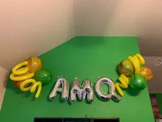 A green wall with a bunch of balloons hanging from it.