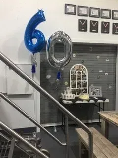 A room with stairs , a table , and balloons in the shape of a number six.