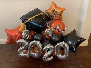 Graduation balloons in black, orange, and silver forming