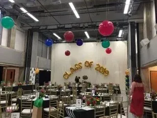 A large room with tables and chairs and balloons hanging from the ceiling.