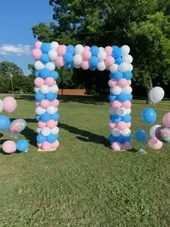 A large arch made of pink and blue balloons in a field.