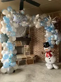 A snowman is standing in front of a balloon arch in a room.