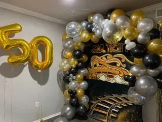 A room decorated with gold , silver and black balloons for a 50th birthday.