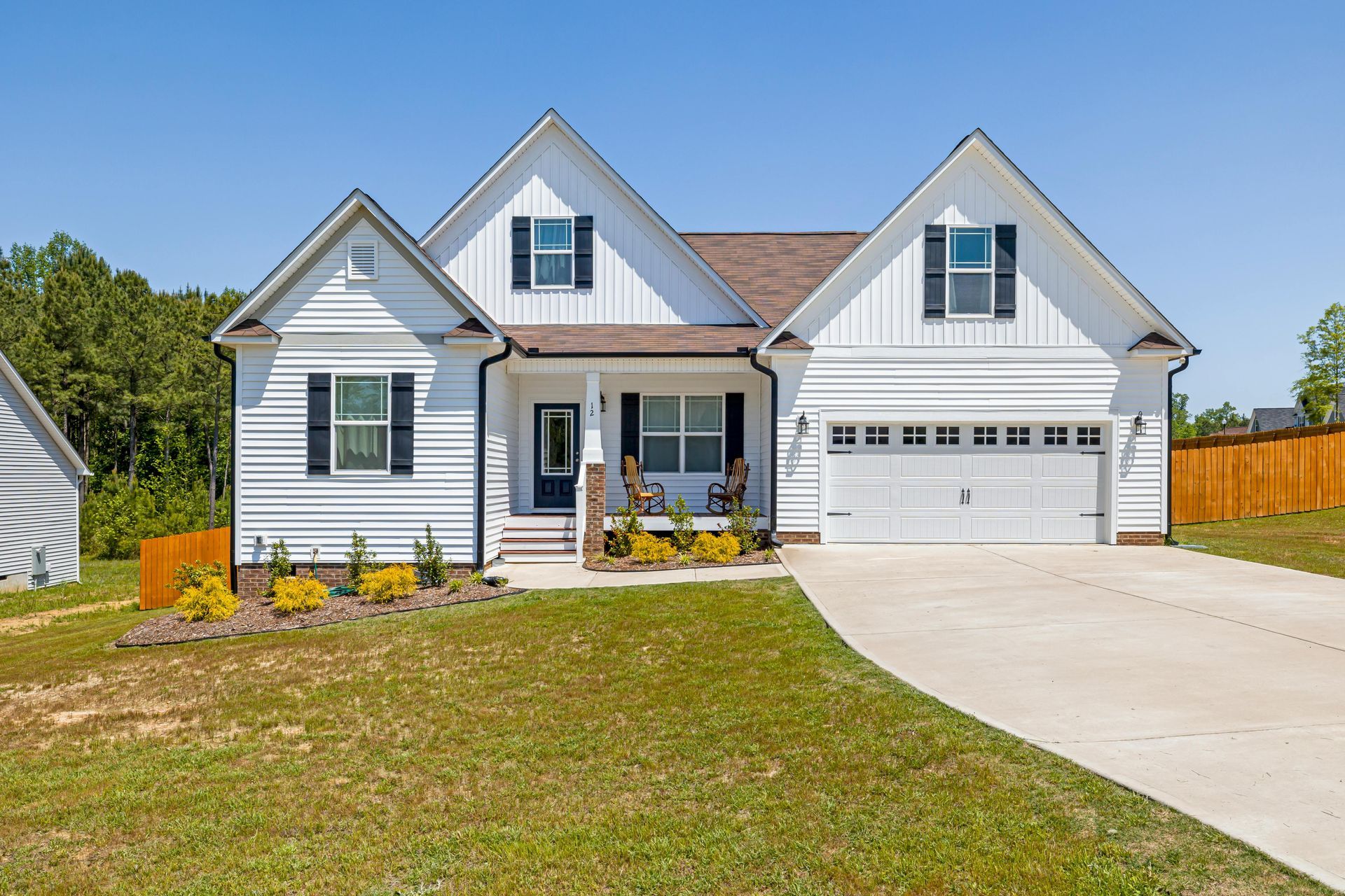 A white house with a brown roof and black shutters is sitting on top of a lush green field.