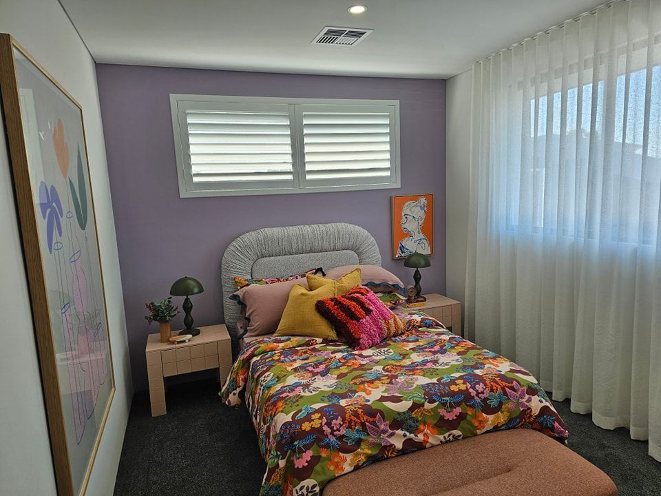 A bedroom with a purple wall and a bed with a colorful comforter
