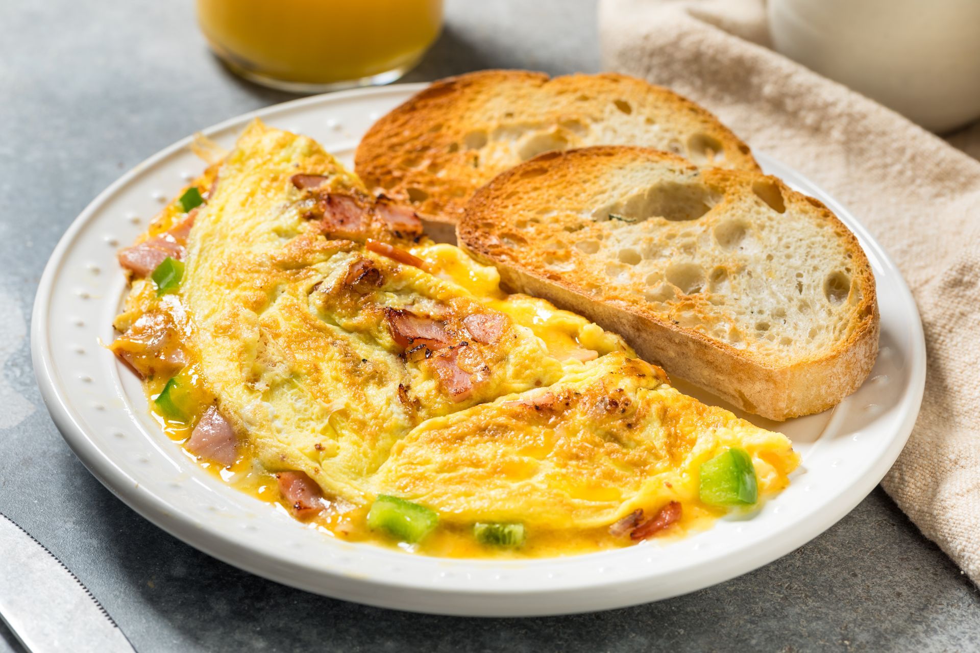 An omelet filled with ham and green peppers served with two slices of toasted bread on a white plate.