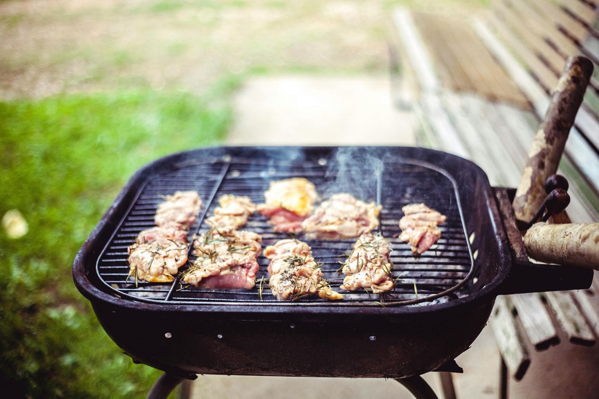 Several pieces of seasoned raw meat cooking on a charcoal grill outdoors.
