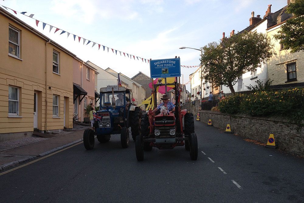 Two tractors are driving down a street in a small town