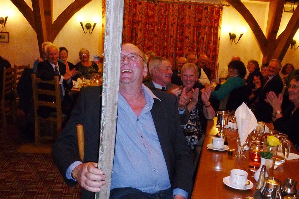 A man is holding a wooden pole in front of a group of people at a table