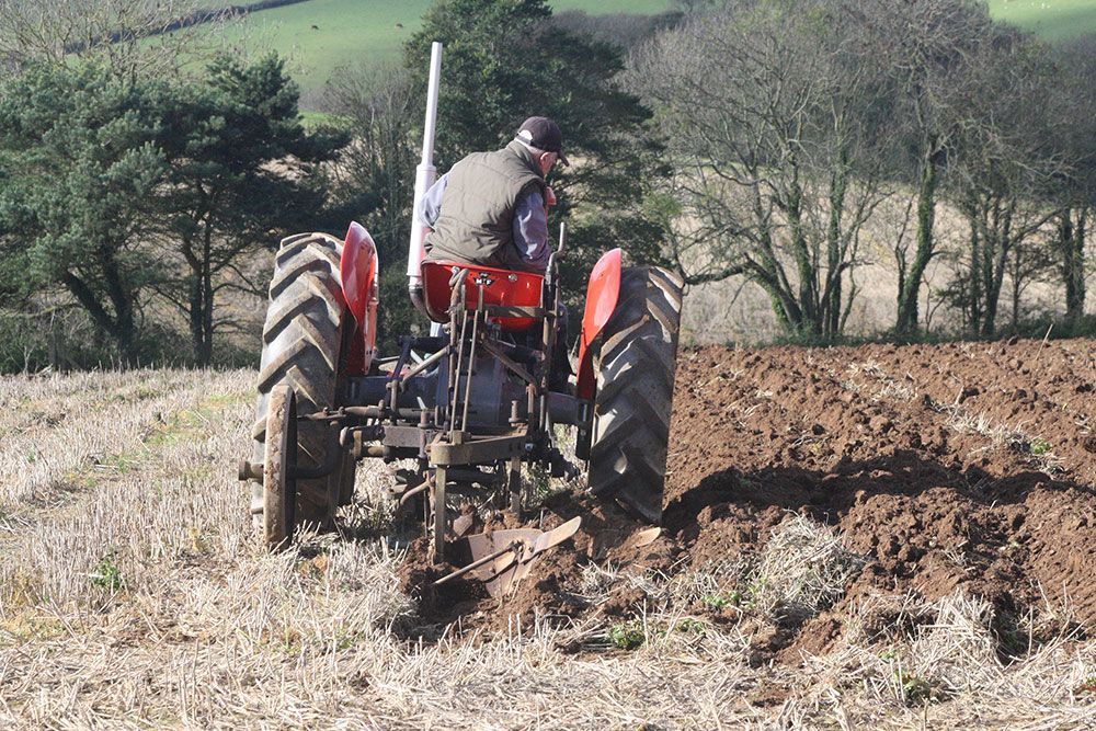 A man is plowing a field with an old tractor