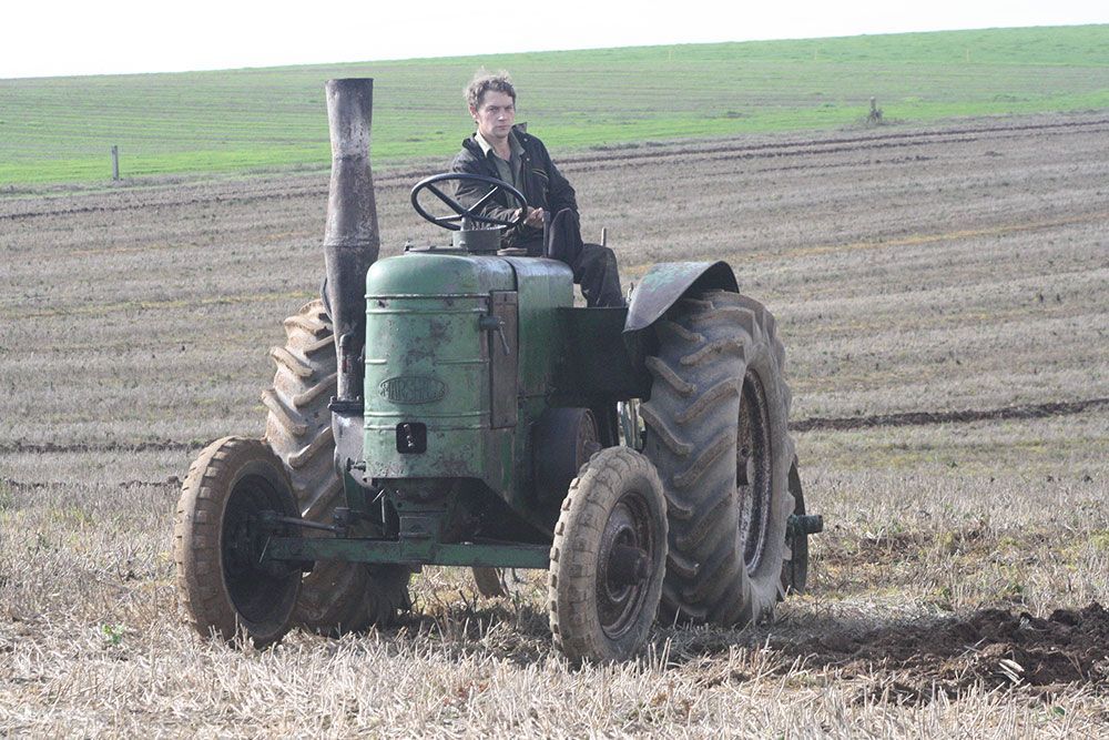 A man is driving an old green tractor in a field.
