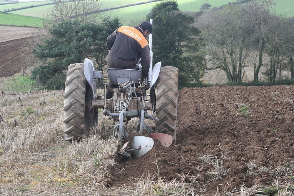 A man is plowing a field with an old tractor