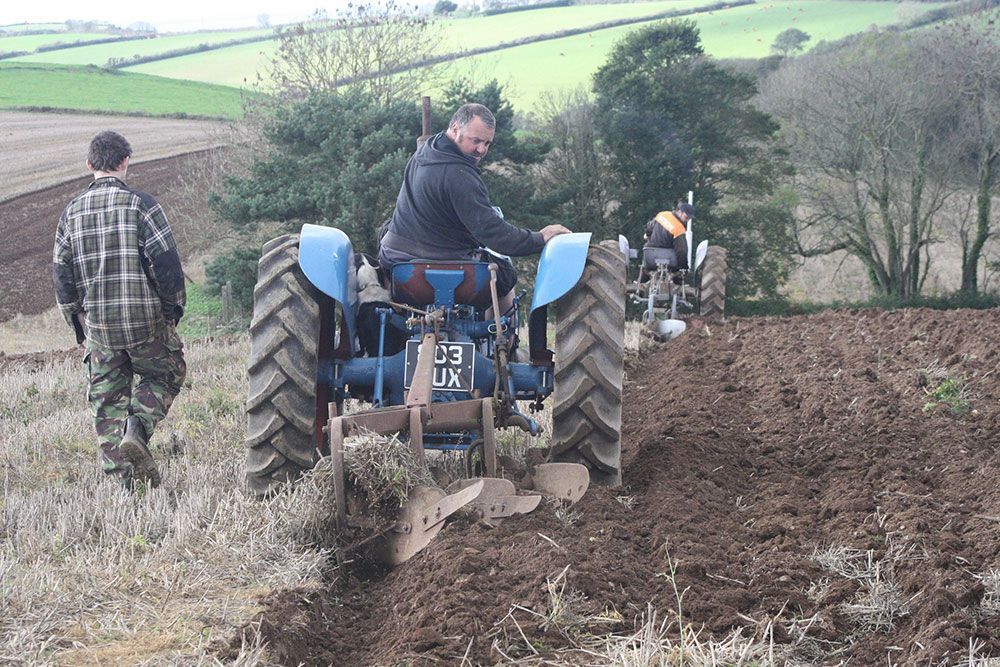 A man is plowing a field with a blue tractor