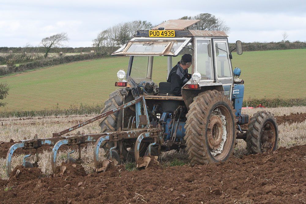 A man is plowing a field with a tractor that has a license plate that says plc 4x2